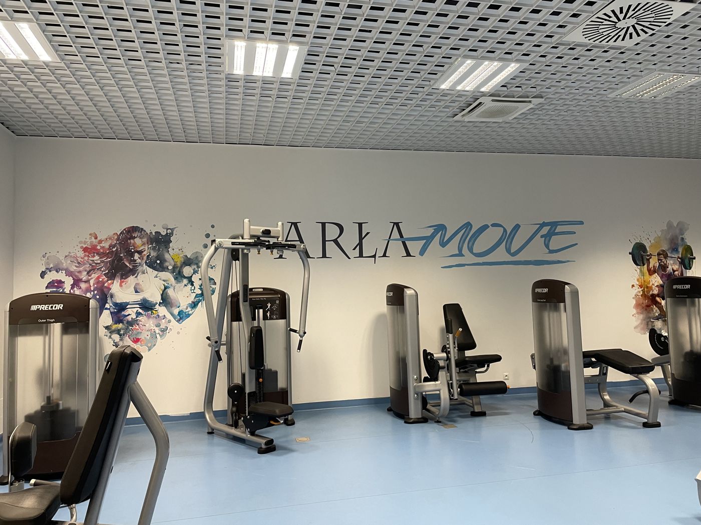 Logo ARŁAMOVE i dwie sylwetki sportowców na ścianie siłowni nad maszynami w Arłamowie