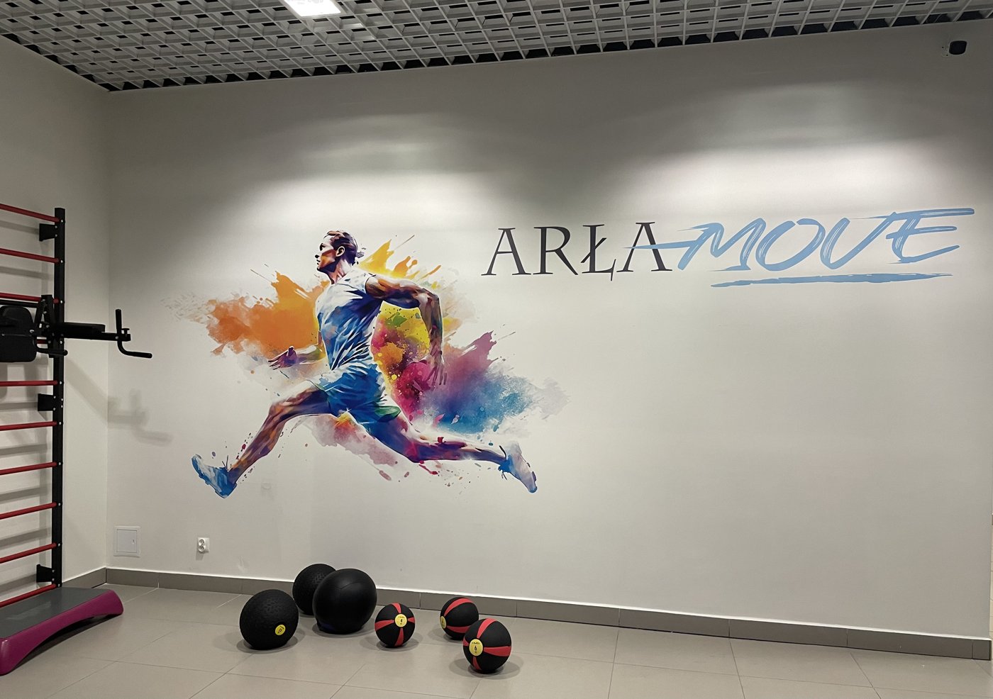 Biegacz w wyskoku i logo ARŁAMOVE na ścianie strefy wejścia w Arłamowie